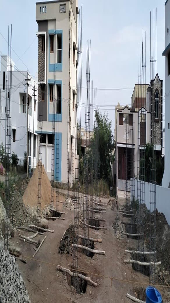 Column starter bars rising from pad footings across a cleared residential plot, with completed houses on either side.